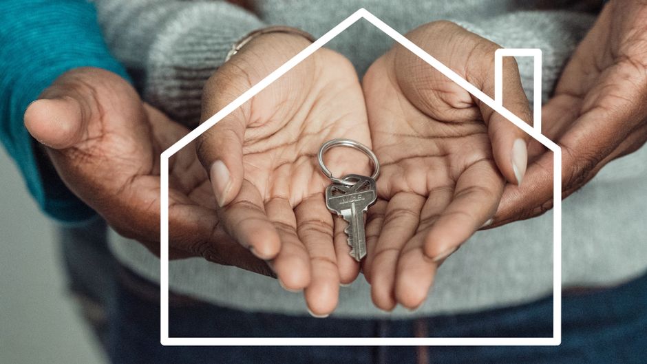 A homeowner's hand holding a set of house keys in front of a modern front door, symbolizing a successful home sale and keeping more equity.