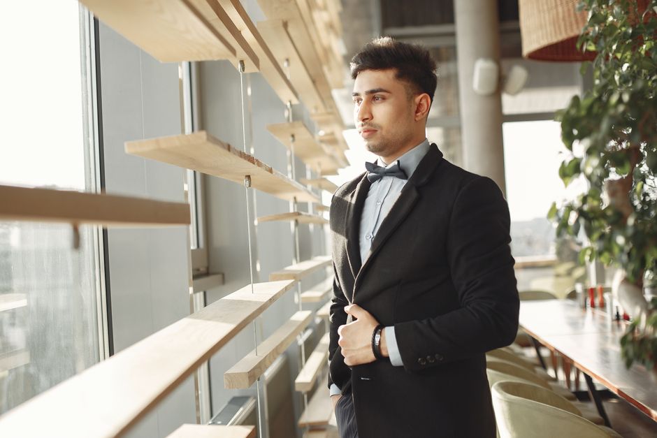 A person in professional attire takes a mindful pause, looking thoughtfully out a large window in a minimalist office, demonstrating a technique for staying centered during a stressful workday.
