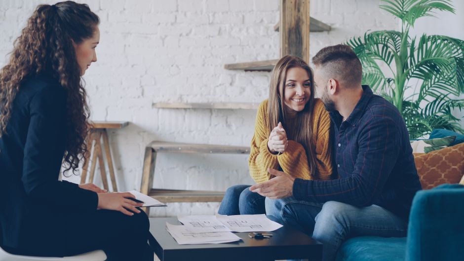 A professional real estate innovator from Columbus, Indiana, discussing options with a smiling couple in a bright, modern office setting.